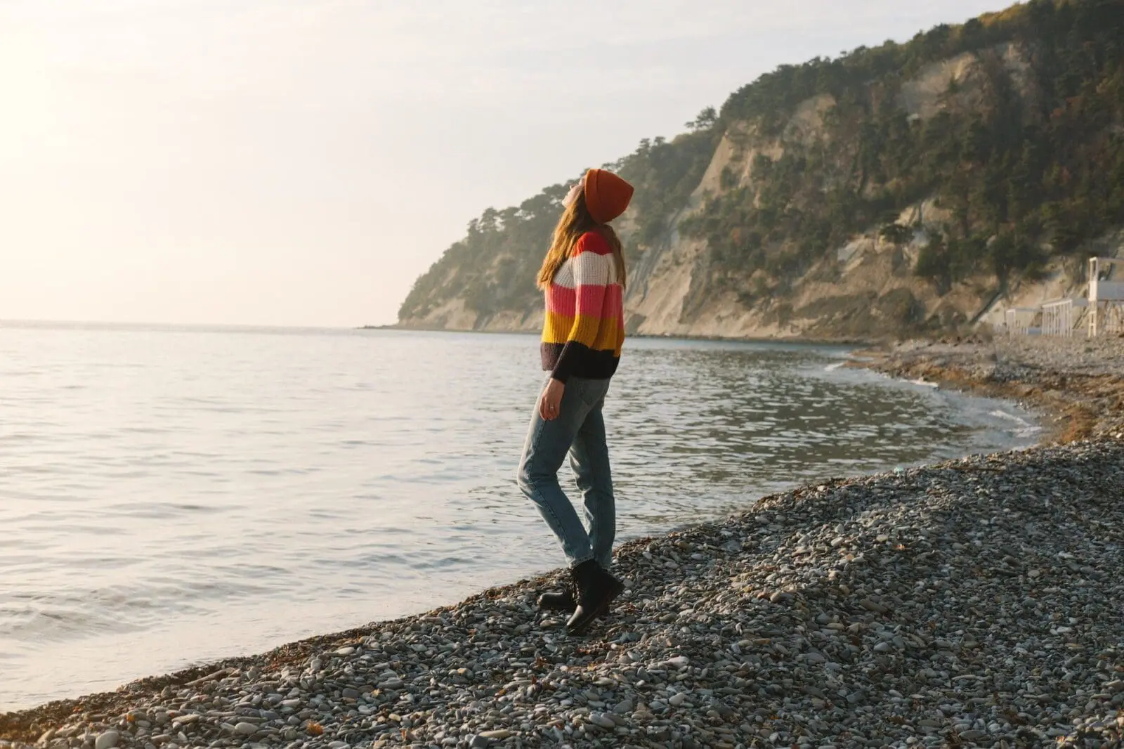 Young beautiful woman in striped sweater stands on the seashore or ocean and enjoy the view. Concept