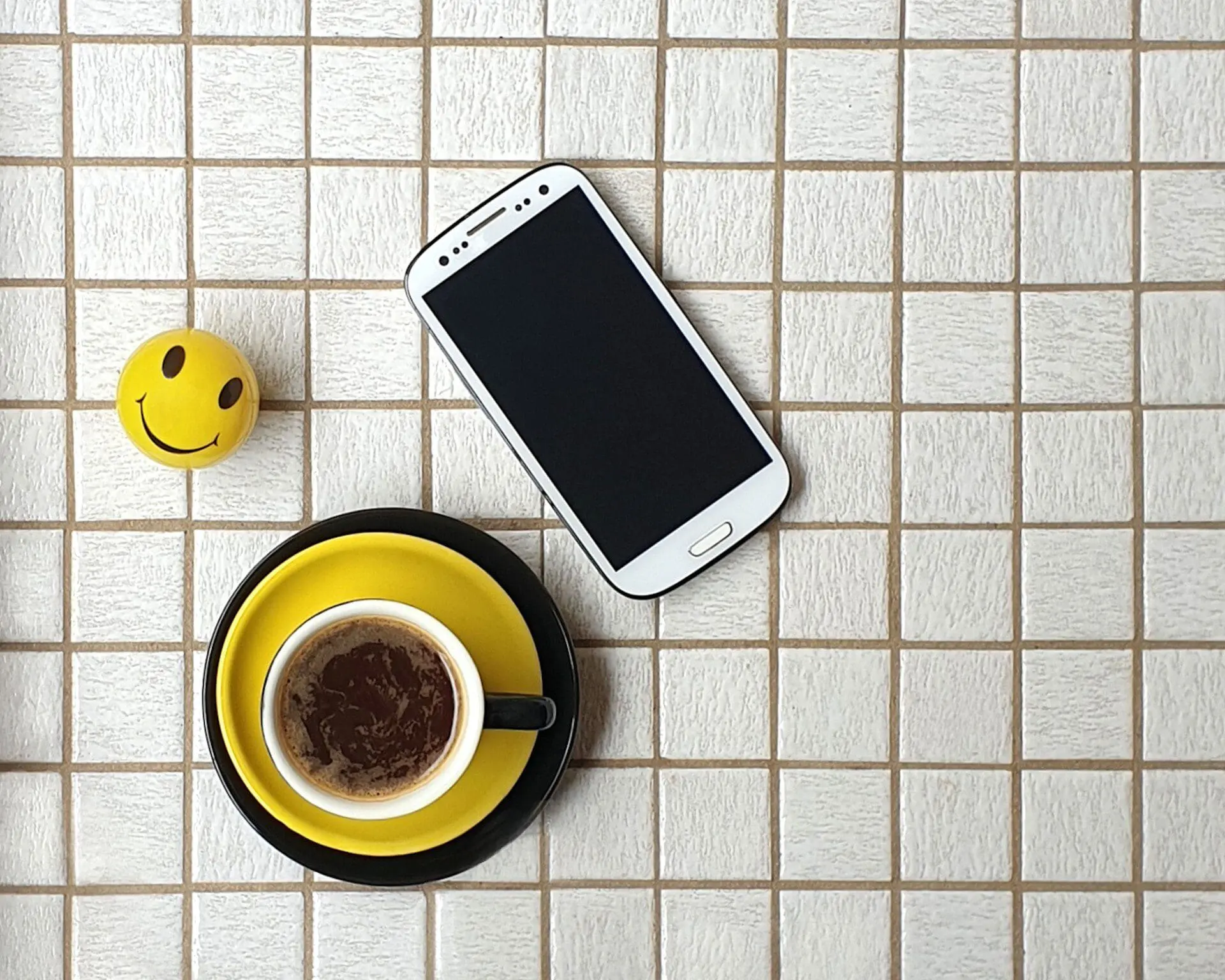 Minimal style coffee with phone on white tiled tabletop