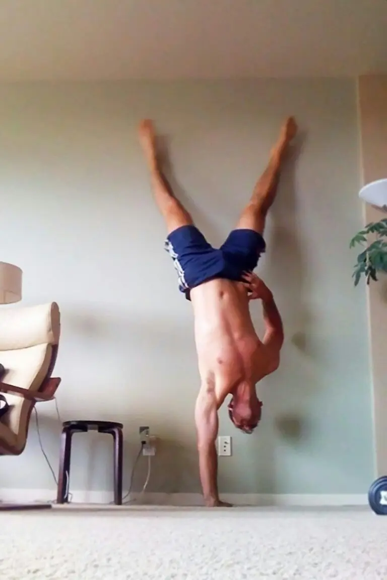 Man working out at home doing a one armed handstand on carpeted living room floor.