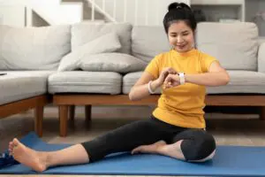 Attractive young woman using smartwatch during yoga stretching yoga online at home. Self-isolation