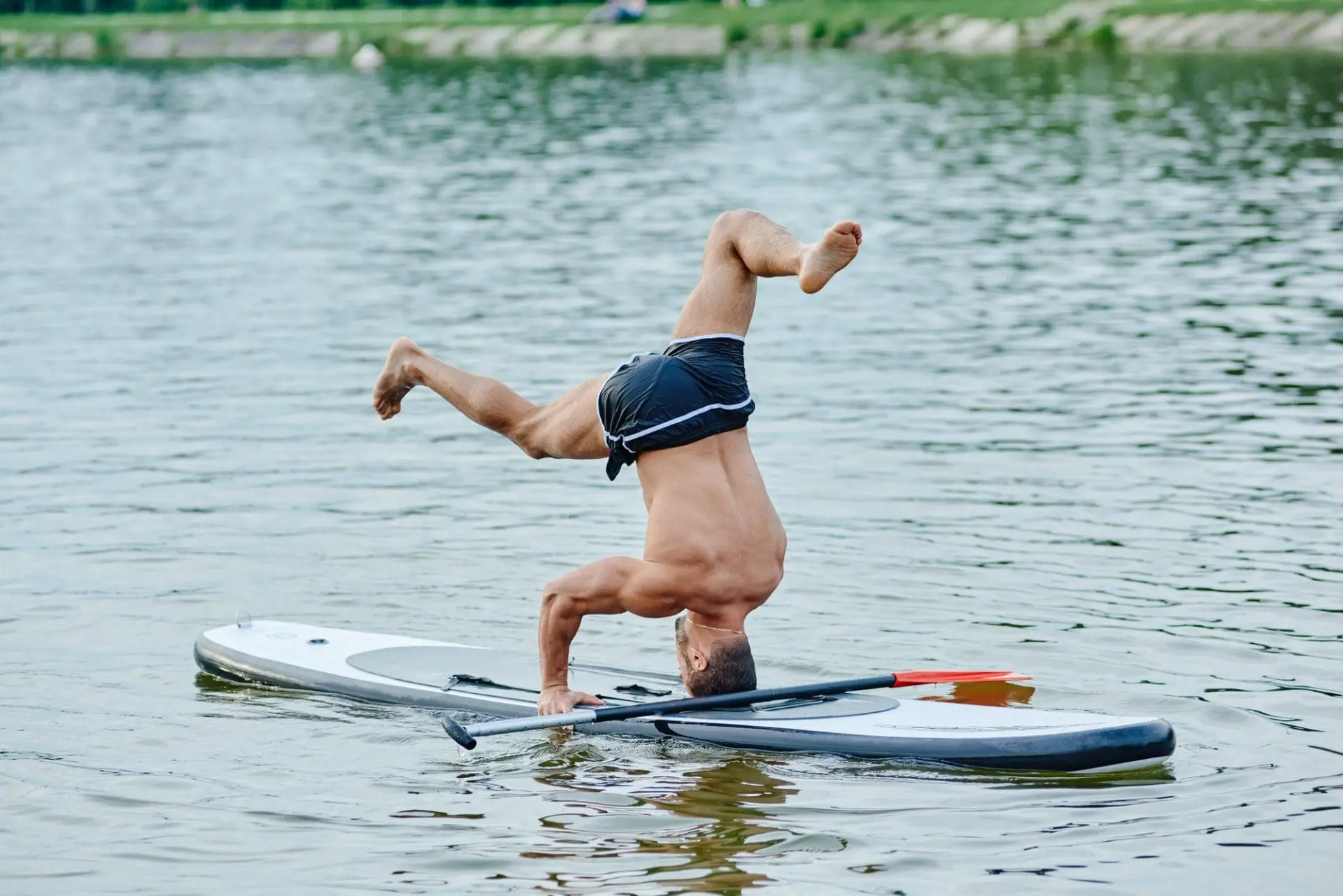 Standing on head, doing yoga exercises, swimming on sup boad in city lake