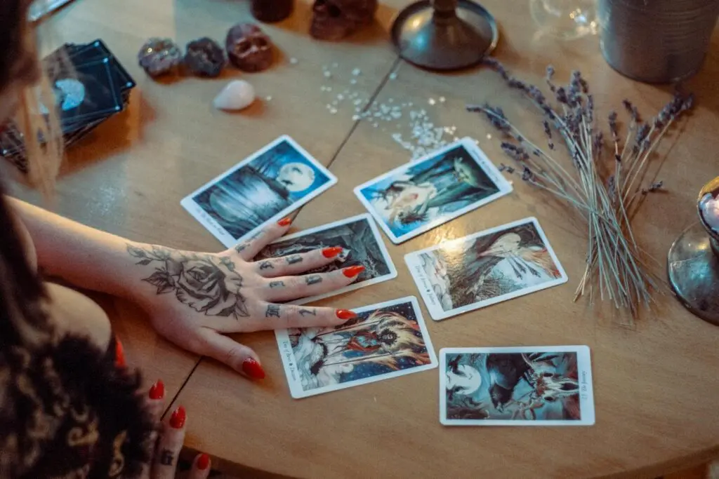 A mystical setup featuring tarot card reading on a wooden table, with artistic tattoos and dried flowers.