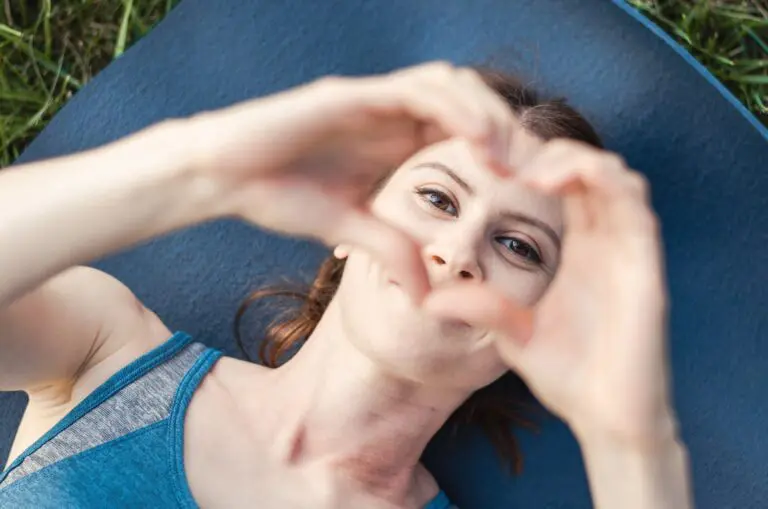 A woman lies on a yoga mat and shows her heart with her hands, top view