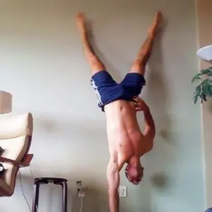 Man working out at home doing a one armed handstand on carpeted living room floor.