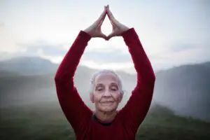 Senior woman doing breathing exercise in nature on early morning with fog and mountains in