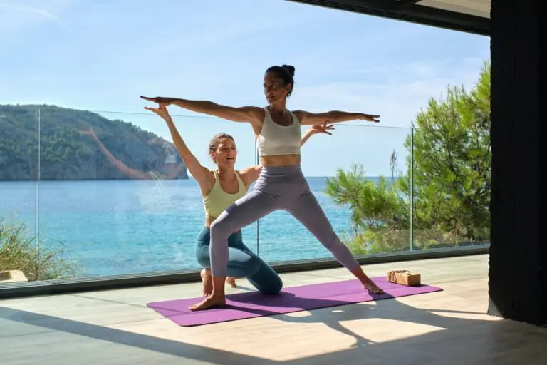 Sportive female performing Warrior pose with help of instructor